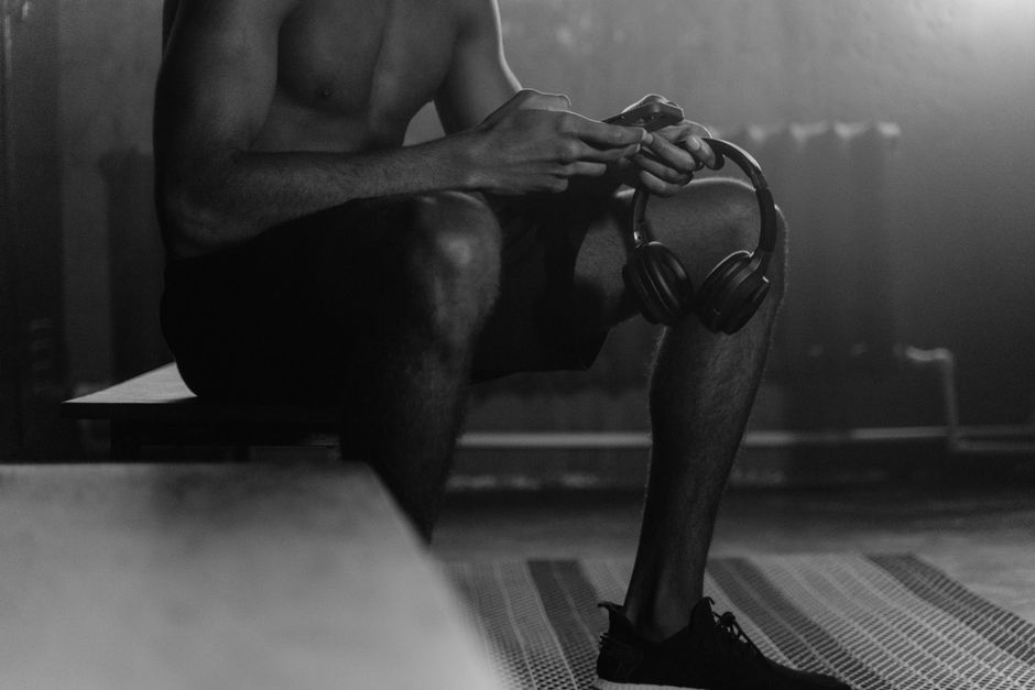 Monochrome photo of a man sitting on a gym bench holding headphones, evoking a quiet and focused atmosphere.