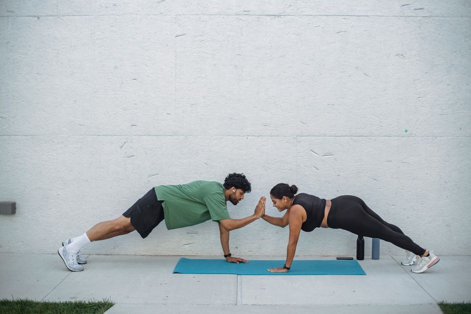 A man and woman perform plank exercises outdoors, promoting fitness and teamwork.