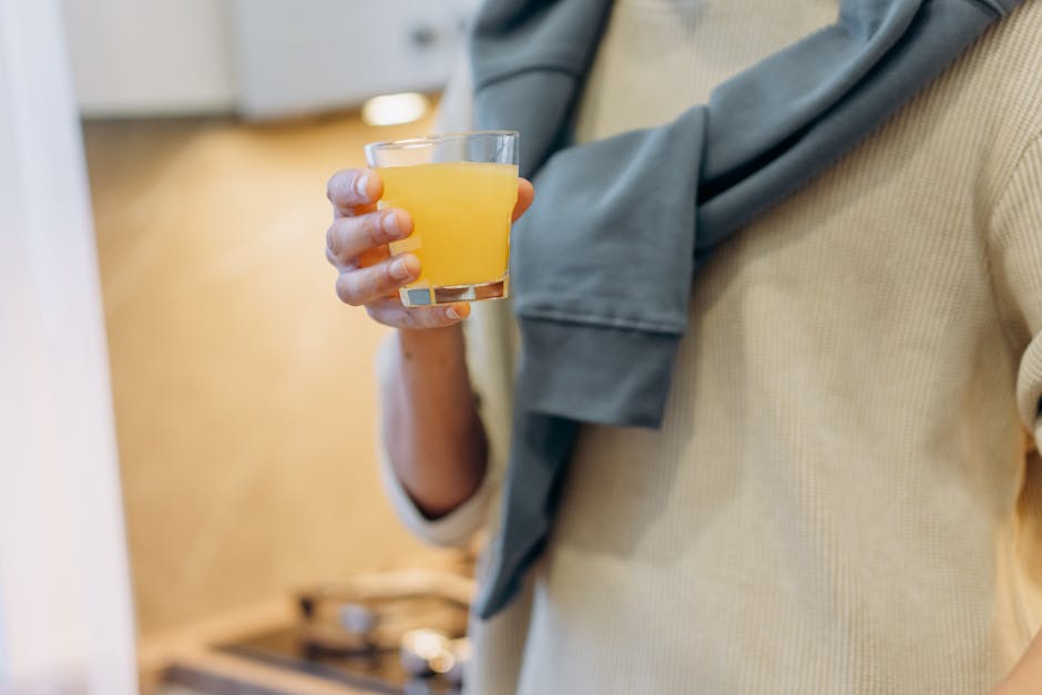Close up of a person holding a glass of orange juice inside a kitchen.