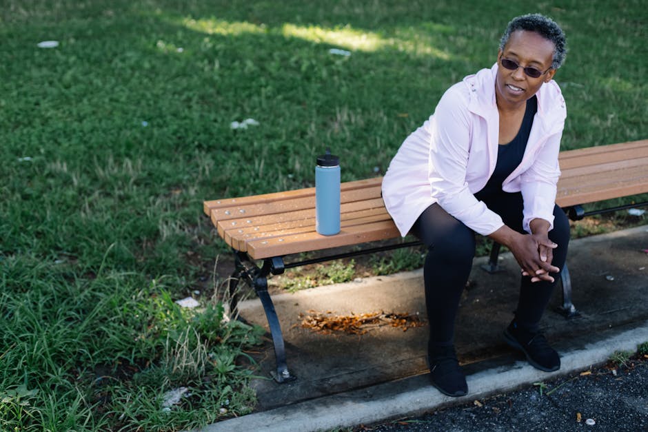 Elderly woman sitting on a park bench with a tumbler, enjoying a peaceful day outdoors.