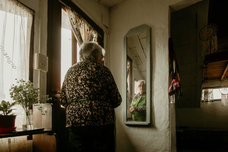 Elderly woman gazes at her reflection in a warm, cozy home setting with decor.