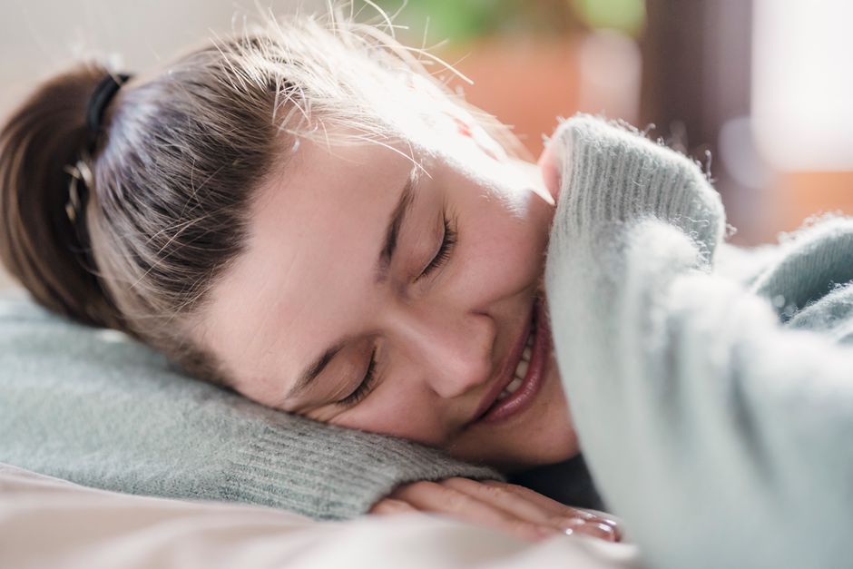 Happy female with closed eyes putting head on hand and smiling while sleeping during weekend morning at home