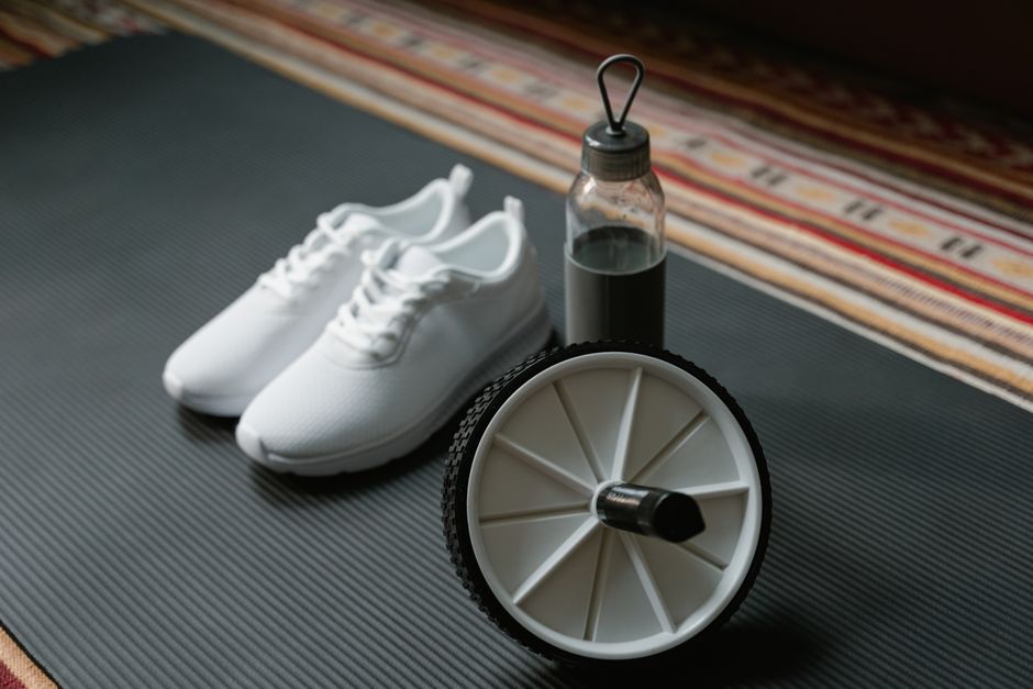 A close-up of white sneakers, ab roller, and water bottle on a yoga mat, ideal for fitness routines.