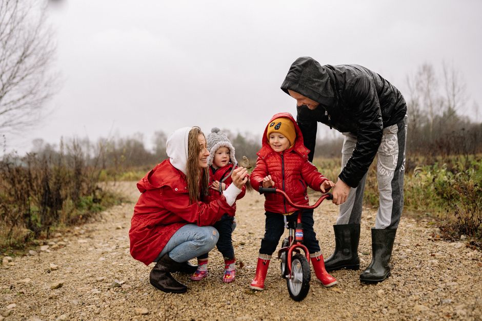 Happy family outdoors with children on a dirt path. Parents supporting kids on a bike ride.