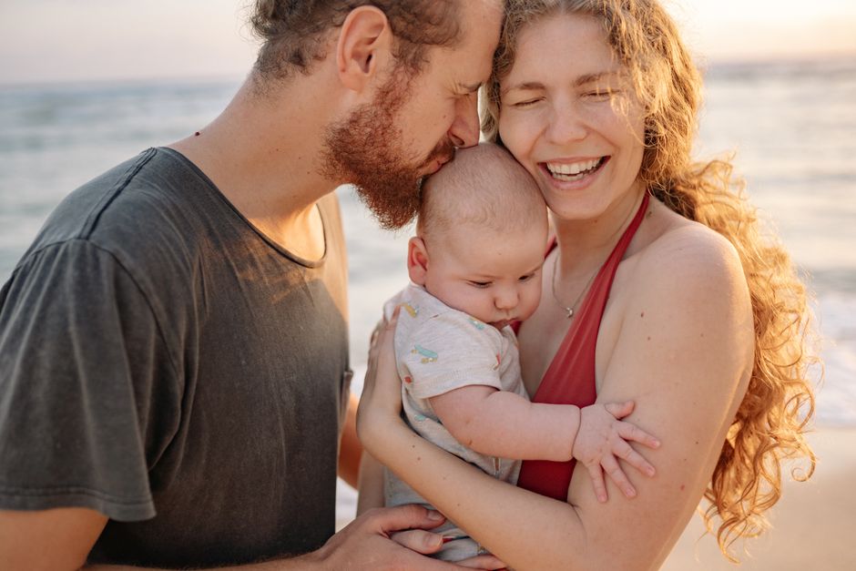 A cheerful family moment with parents and baby by the seaside, embracing love and connection.