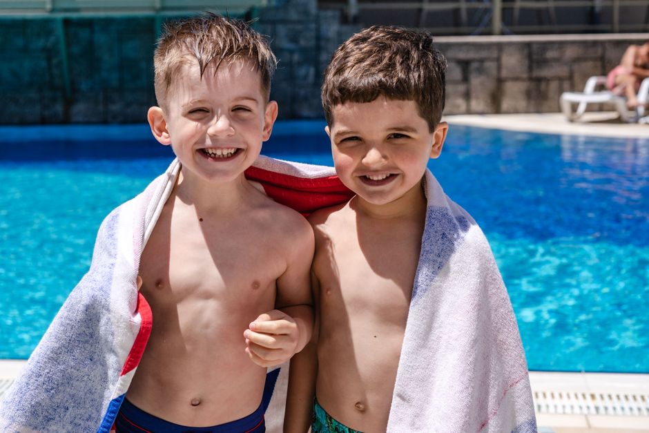 Two smiling boys wrapped in towels enjoying a sunny day by the swimming pool.