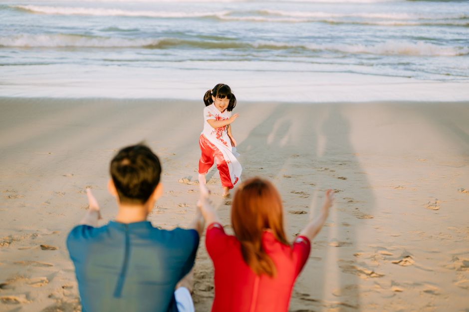 Joyful family moment with child running to parents on a sandy beach during sunset.
