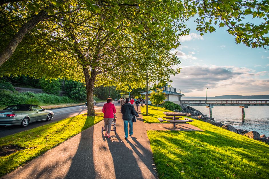 A peaceful riverside walkway with people enjoying a stroll in the bright afternoon.