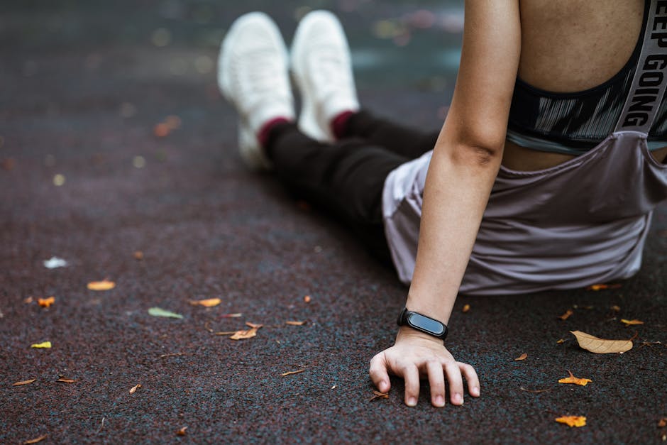 Back view of anonymous female in sportswear and smart watch resting after exercising on sports ground
