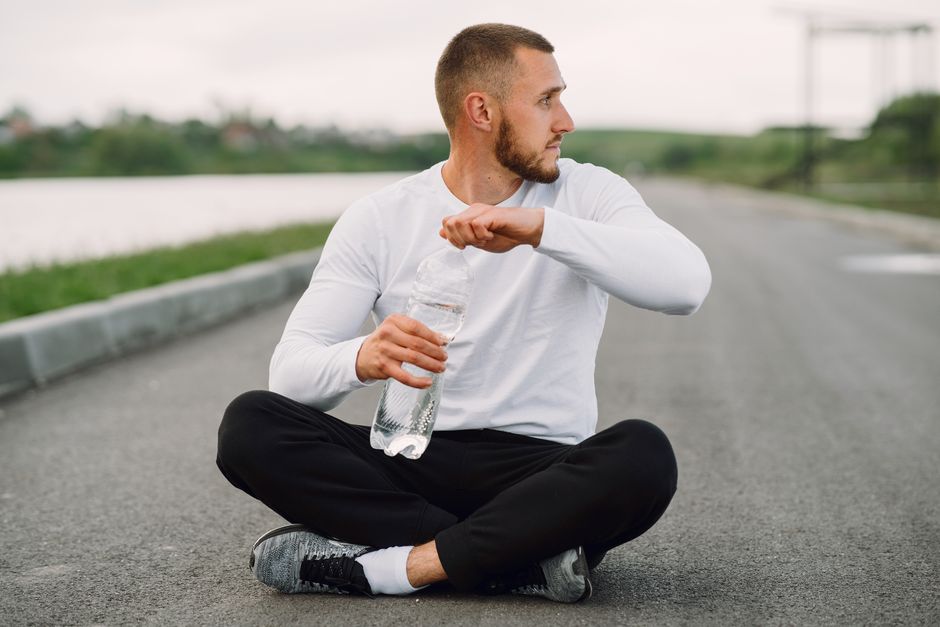 Man seated on an empty road holding a water bottle, focusing on healthy lifestyle.