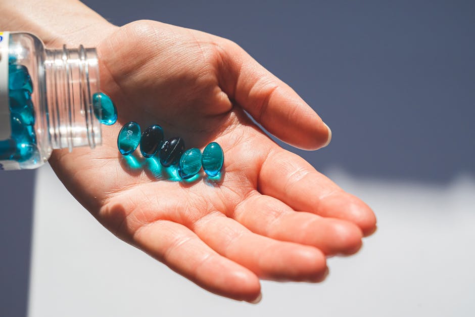 Blue gel capsules pouring from a bottle into an open hand, showcasing medication concept.