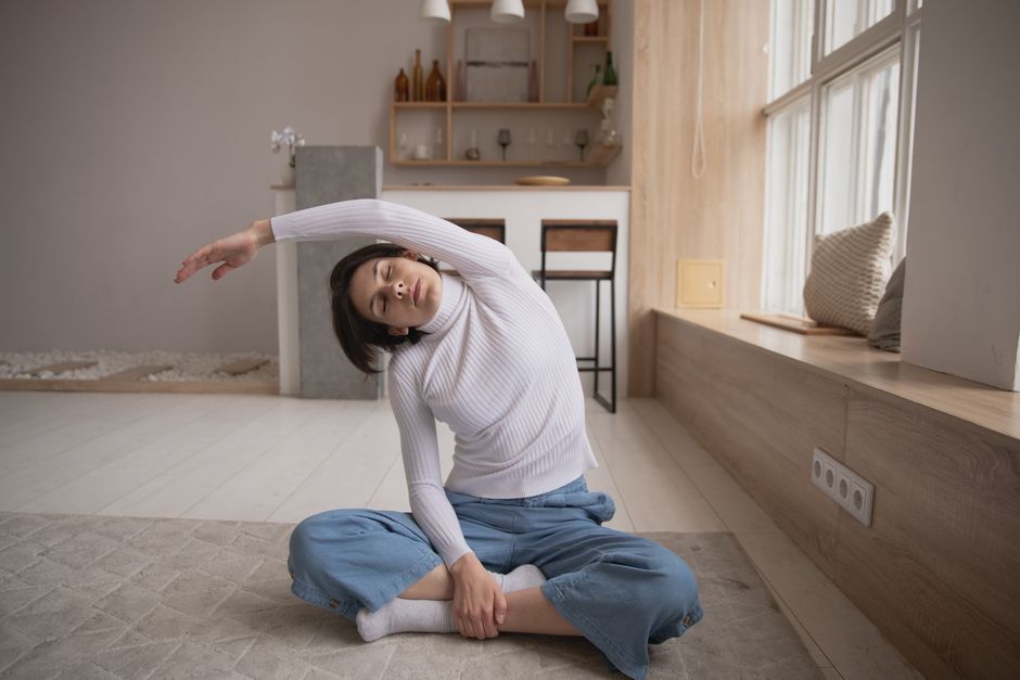 Woman performing a side stretch yoga pose indoors, emphasizing relaxation and fitness in a cosy setting.