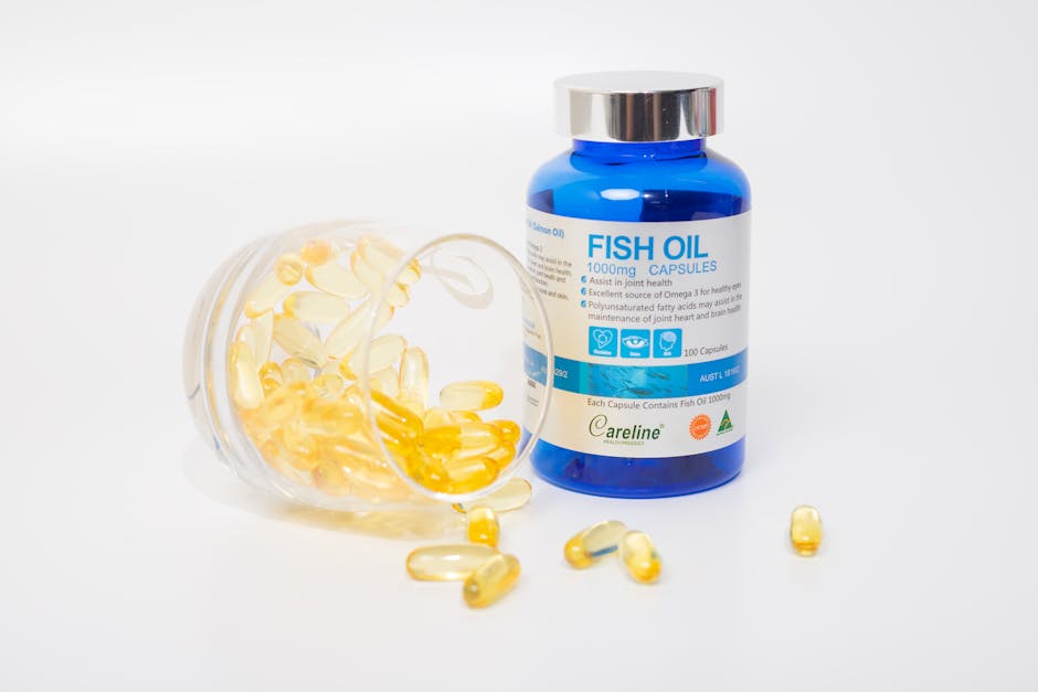 Fish oil capsules spilling out of a container next to a blue bottle on a white background.