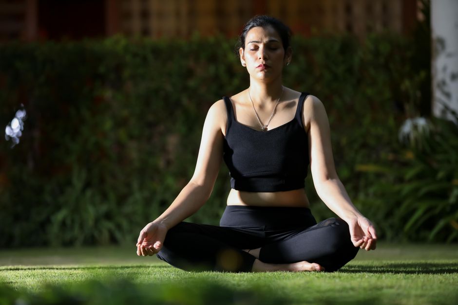 Calm woman in black outfit meditating outdoors, sitting cross-legged on grass.