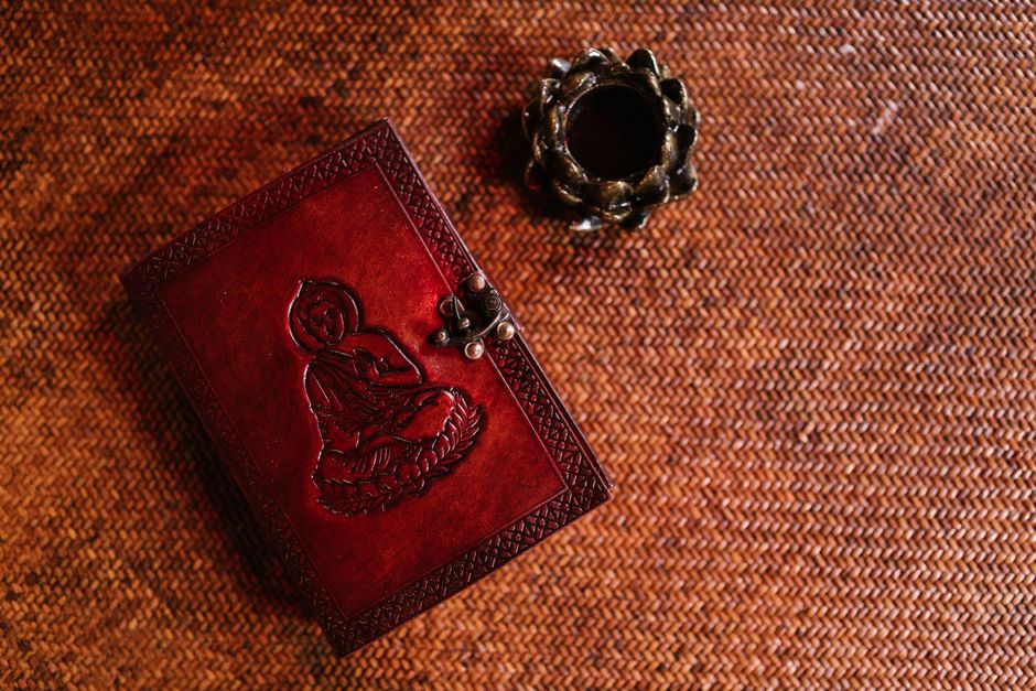 Elegant leather book with Buddha engraving beside a decorative candle on textured background.