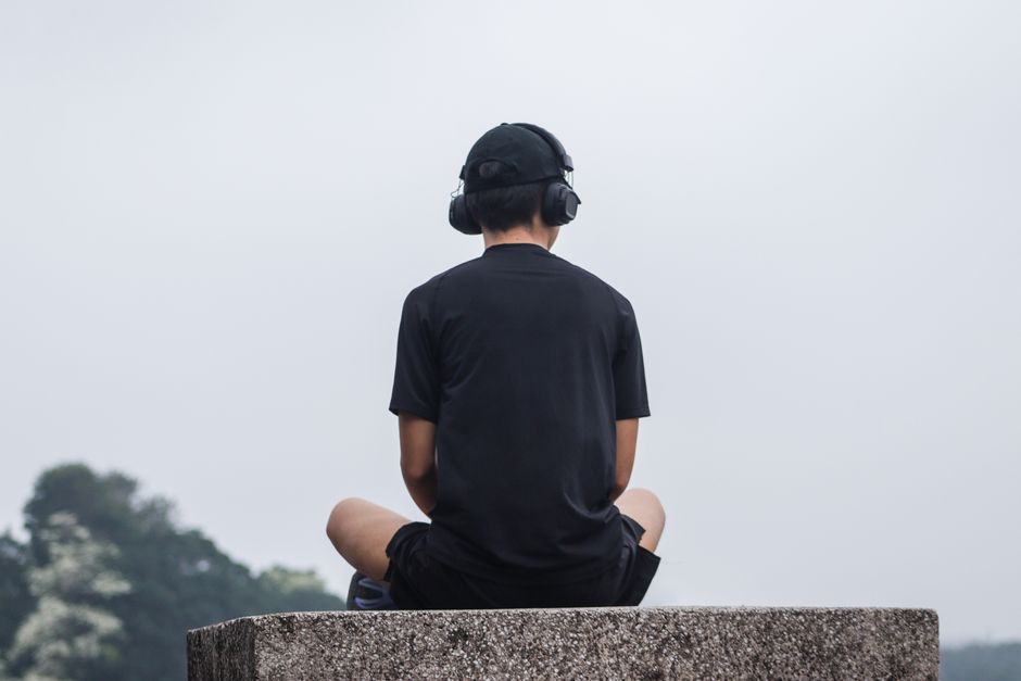 A teenager sitting cross-legged outdoors, meditating with headphones for relaxation.