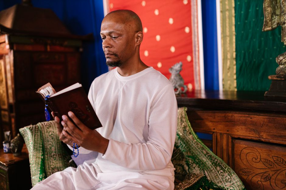Adult man in white robe meditating while reading a holy book in a serene Buddhist temple setting.