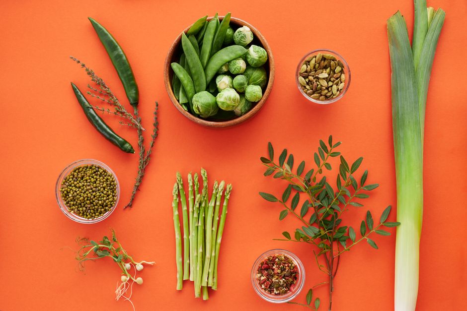 Top view of assorted green vegetables and herbs on a bold orange background, showcasing freshness.