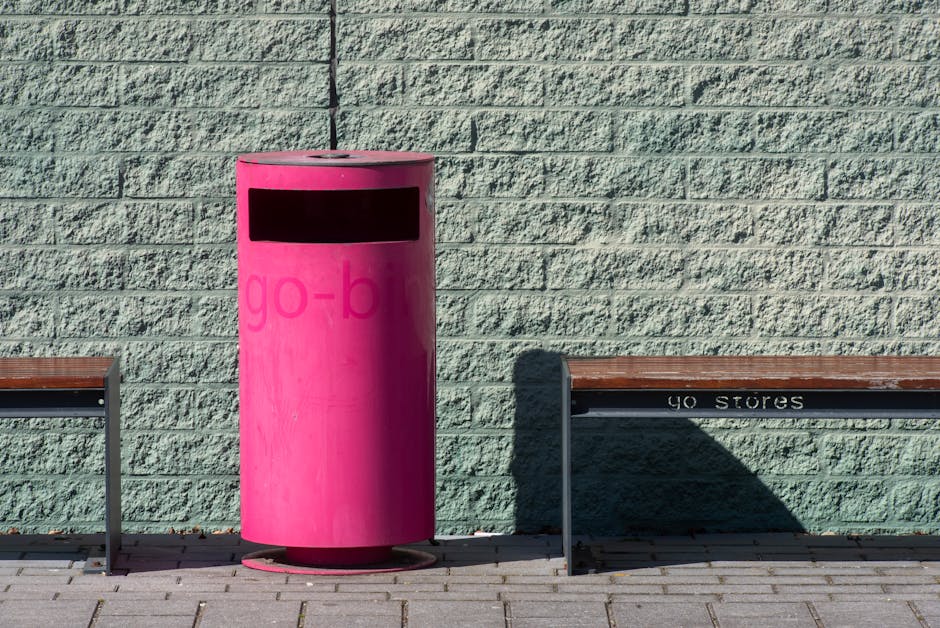 Bright pink trash bin and bench against a light blue brick wall, emphasizing urban design.