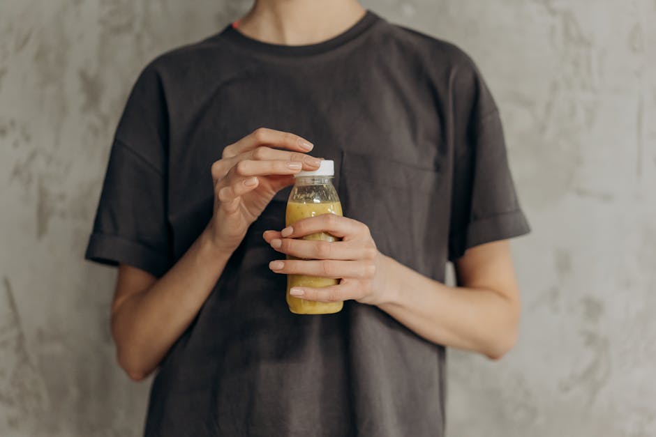 Close-up of individual in dark shirt holding a plastic bottle of juice against a textured wall.