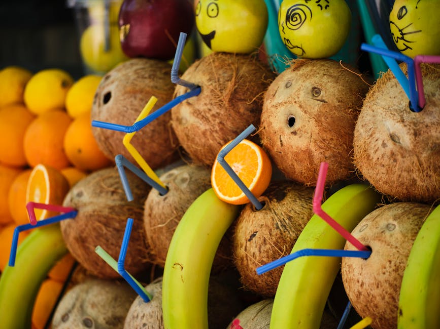 A vibrant arrangement of coconuts, bananas, and oranges with fun decorations, showcasing tropical freshness.