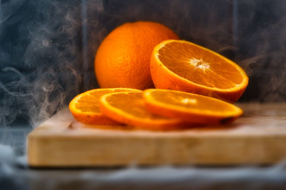 Vibrant fresh orange slices arranged on a wood cutting board with a misty steam effect in the background.