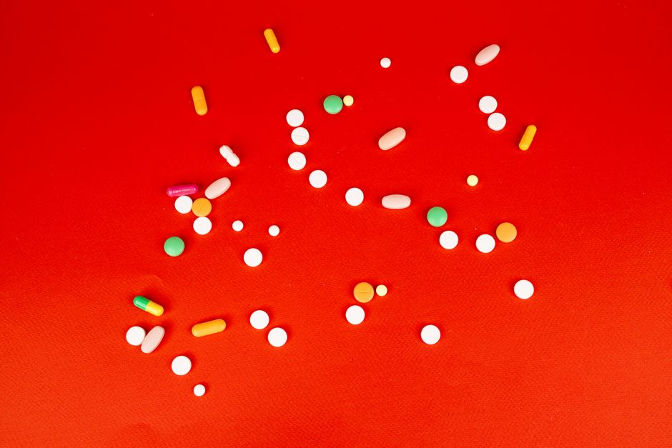 A colorful assortment of pills and capsules scattered on a bright red surface. Healthcare and medication concept.