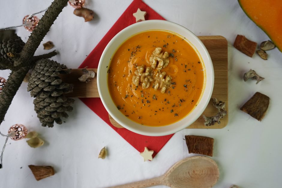 Delicious creamy pumpkin soup with walnuts, styled with autumn elements, captured in a flat lay.
